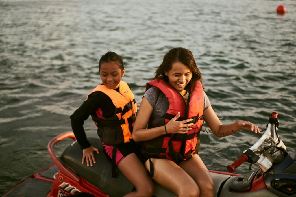 a woman and a girl wearing life vests riding on red jetski