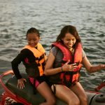 a woman and a girl wearing life vests riding on red jetski