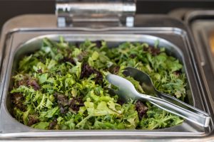 green vegetable salad in stainless steel food tray with stainless tongs