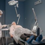 nurse with face mask standing by patient on bed in operating room