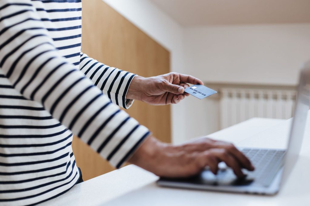 a side view of a senior male hands holding a credit card and typing on a laptop