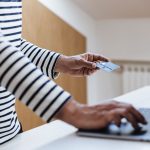 a side view of a senior male hands holding a credit card and typing on a laptop