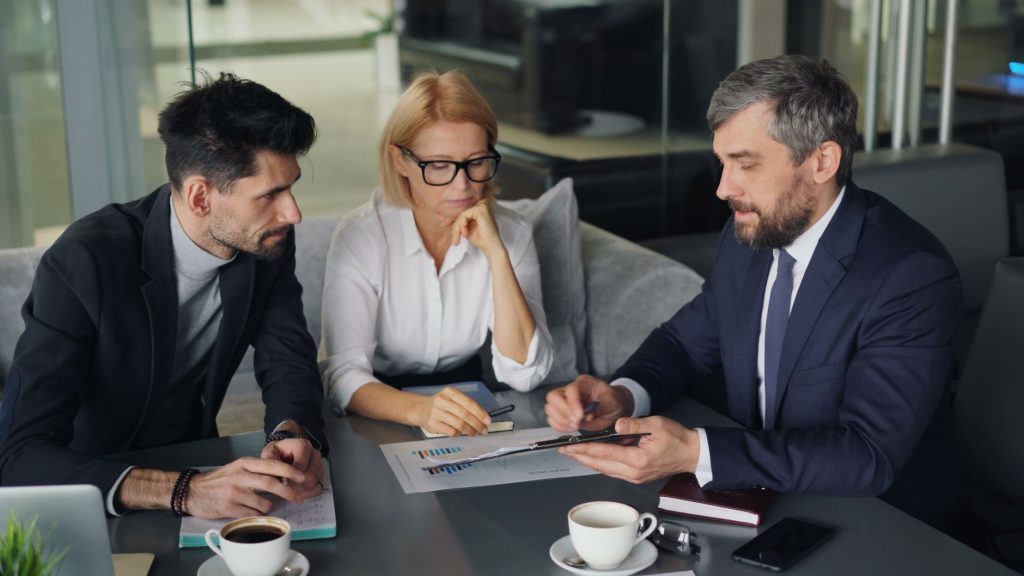 three business people sitting at a table with a laptop