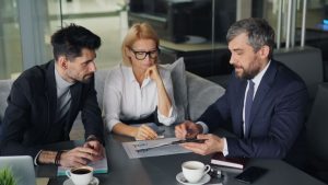 three business people sitting at a table with a laptop