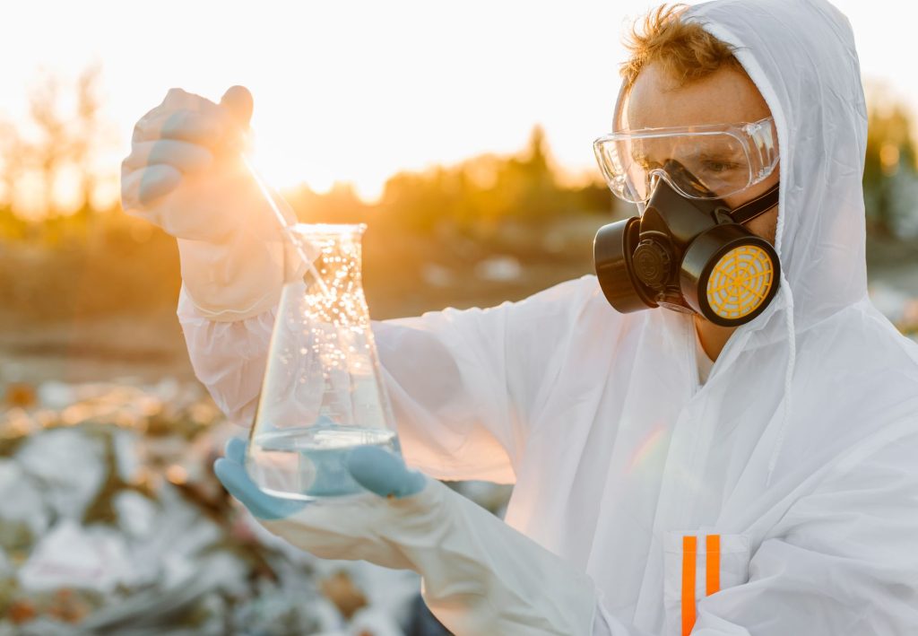 person in ppe on a dumpsite holding an erlenmeyer flask